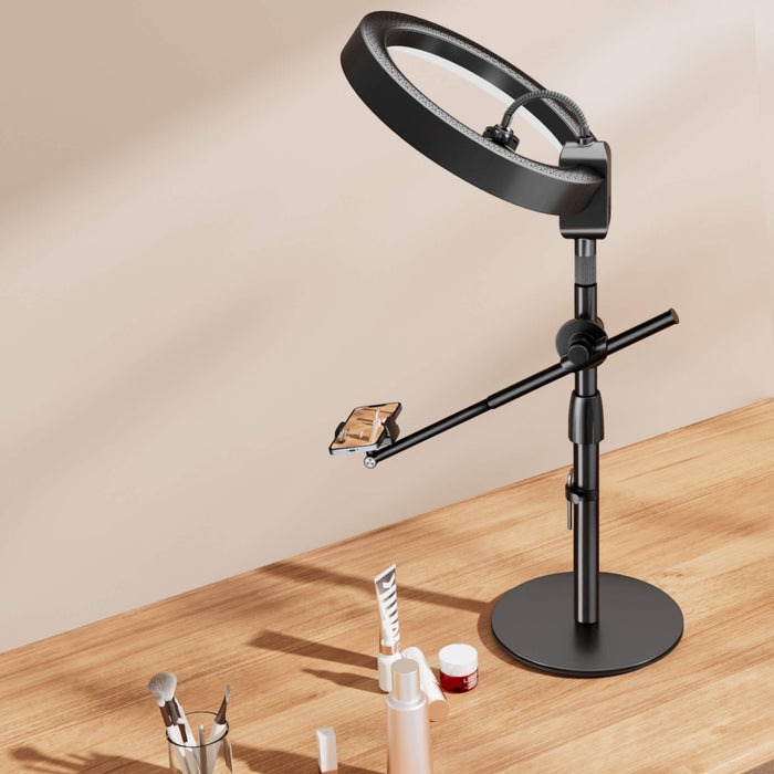 Black ring light stand on a wooden table, equipped with a phone holder, ideal for makeup tutorials.